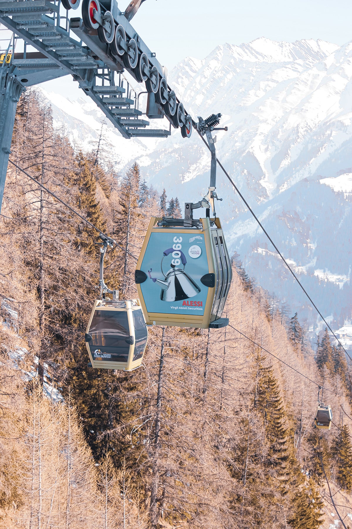 Alessi-branded gondola glides over snowy Alps, pine forests, and mountain peaks in Courmayeur, 2023.
