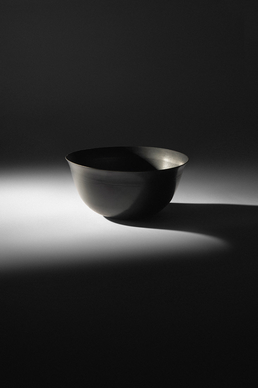 Sleek black ceramic bowl illuminated by soft spotlight, casting dramatic shadow on dark surface.