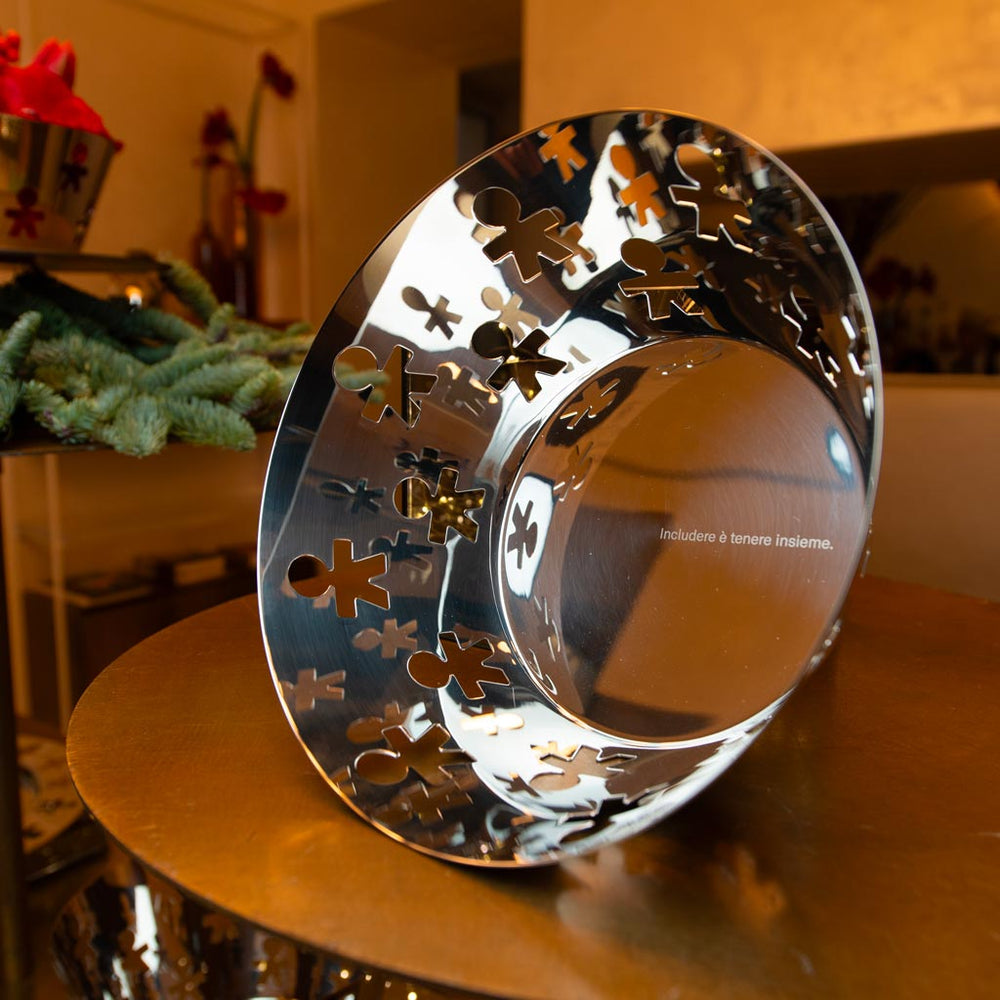 Shiny metallic bowl with cutout human figures, reflecting warm light, displaying Italian text "Includere è tenere insieme" — symbolizing connection and inclusivity.