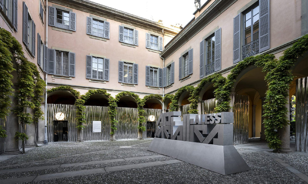 Sleek gray "Alessi" sculpture in ivy-covered courtyard, Milan Design Week 2023, modern art meets historic architecture.