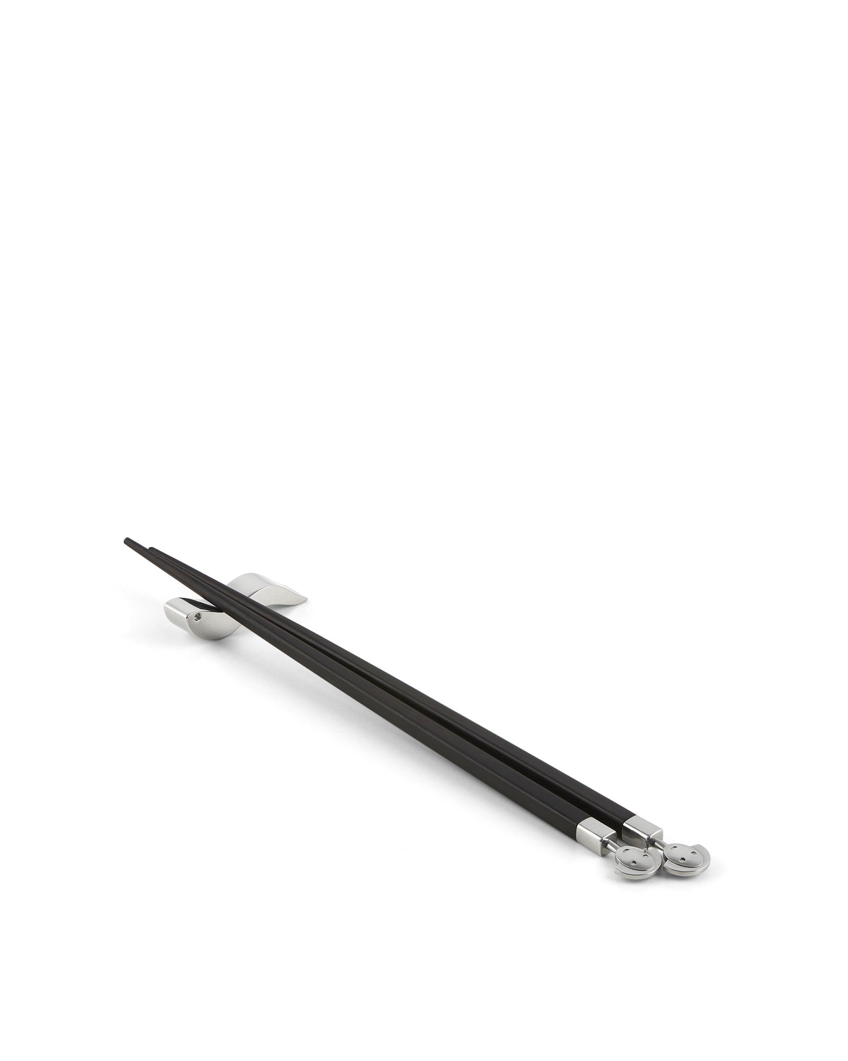Black chopsticks with silver accents by Alessi, resting on silver chopstick rests, featuring smiling face details.