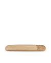 A light brown wooden serving plate by Alessi with an ornate geometric pattern etched on one end.