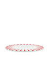 White Christmas decorative plate by Alessi with red sunburst rays and gold stars, angled view.