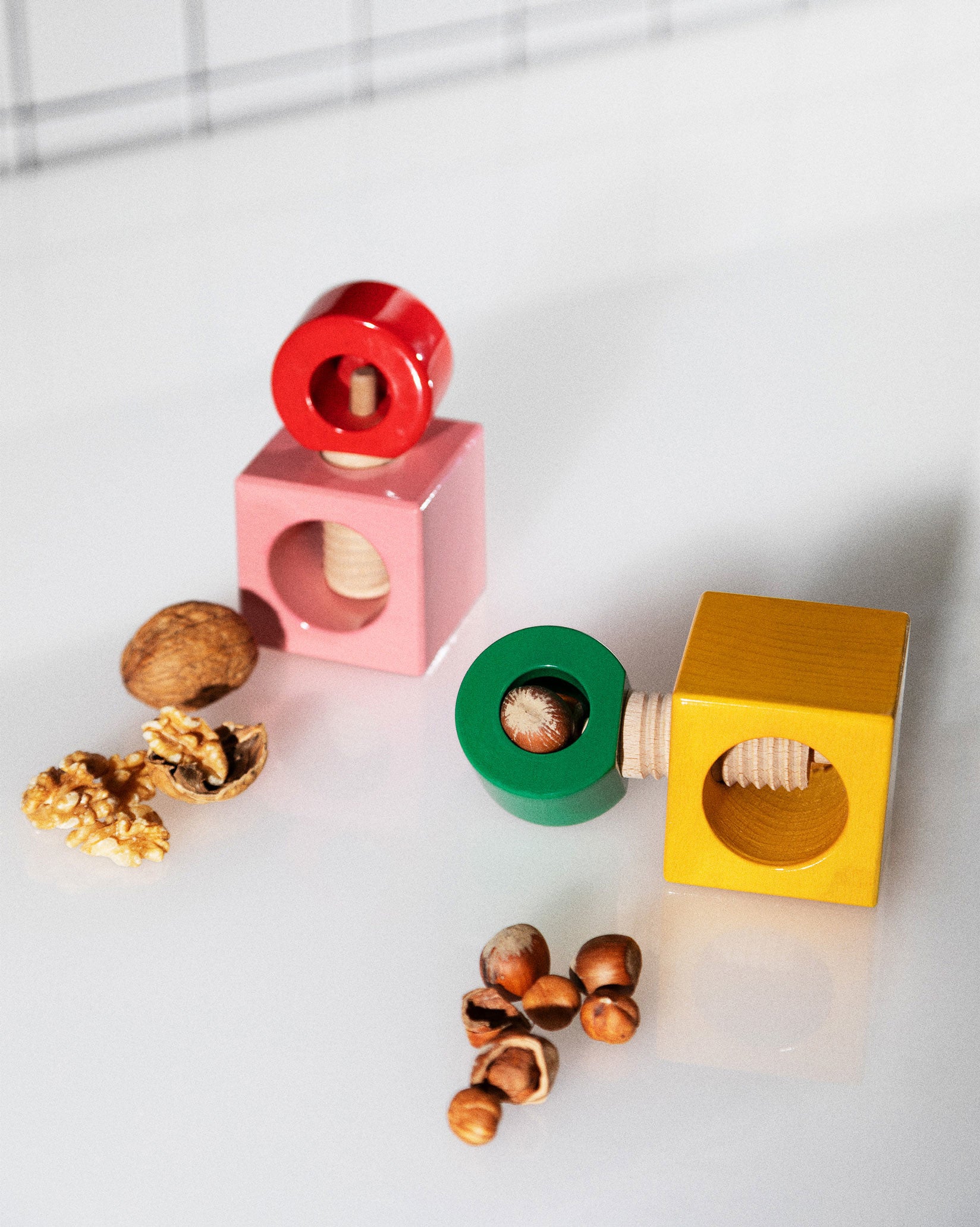 Colorful wooden nutcrackers by Alessi, two block designs in red/pink and green/yellow, with walnuts and hazelnuts.