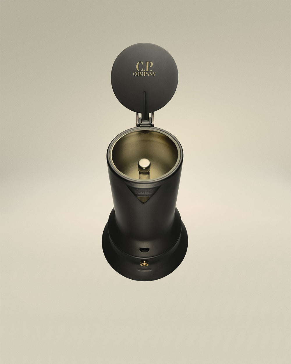 Dark grey espresso coffee maker by Alessi with lid open, revealing gold interior and 'C.P. COMPANY' text.