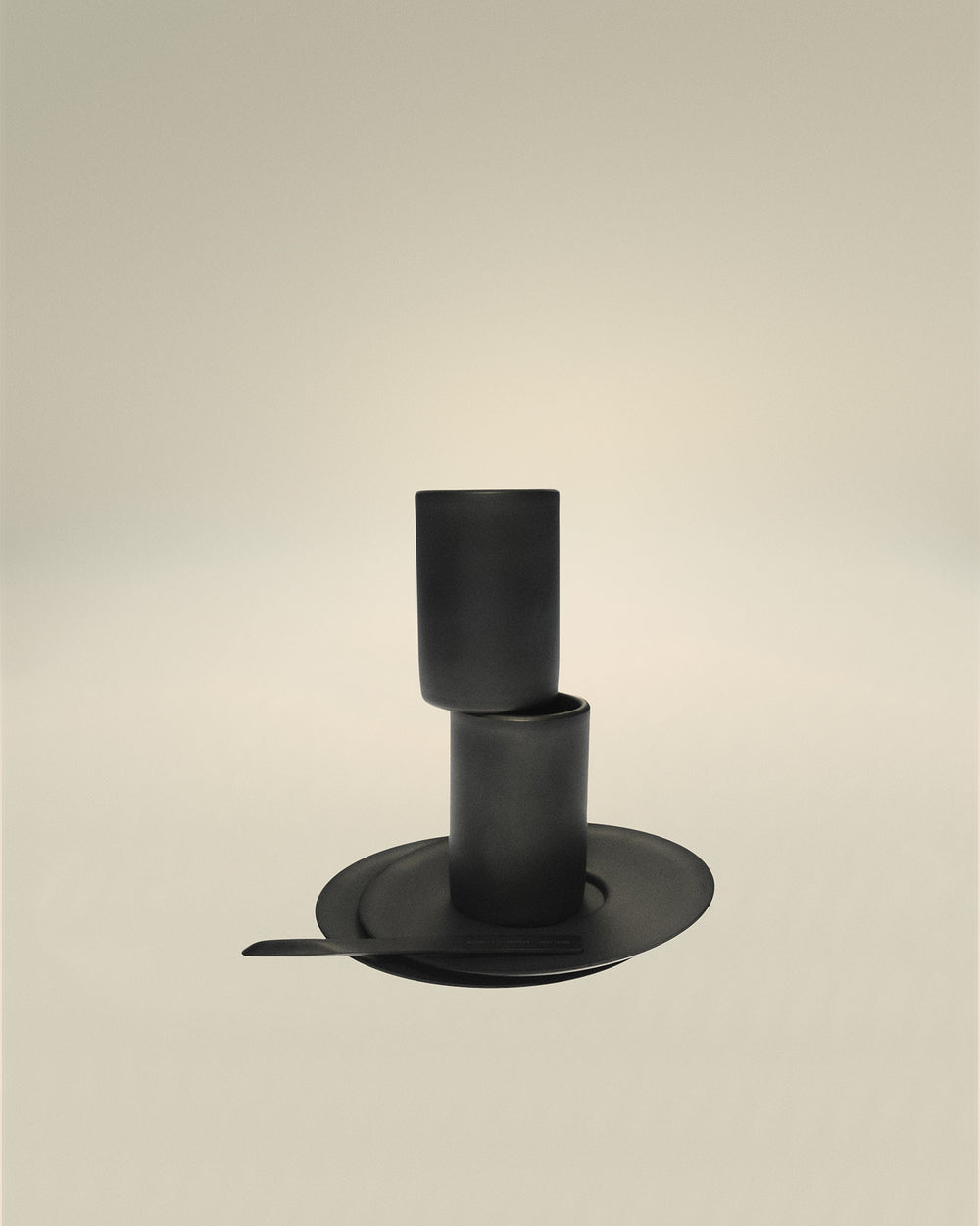 Matte black ceramic cups by Alessi, stacked vertically on a matching saucer with a stirring stick.