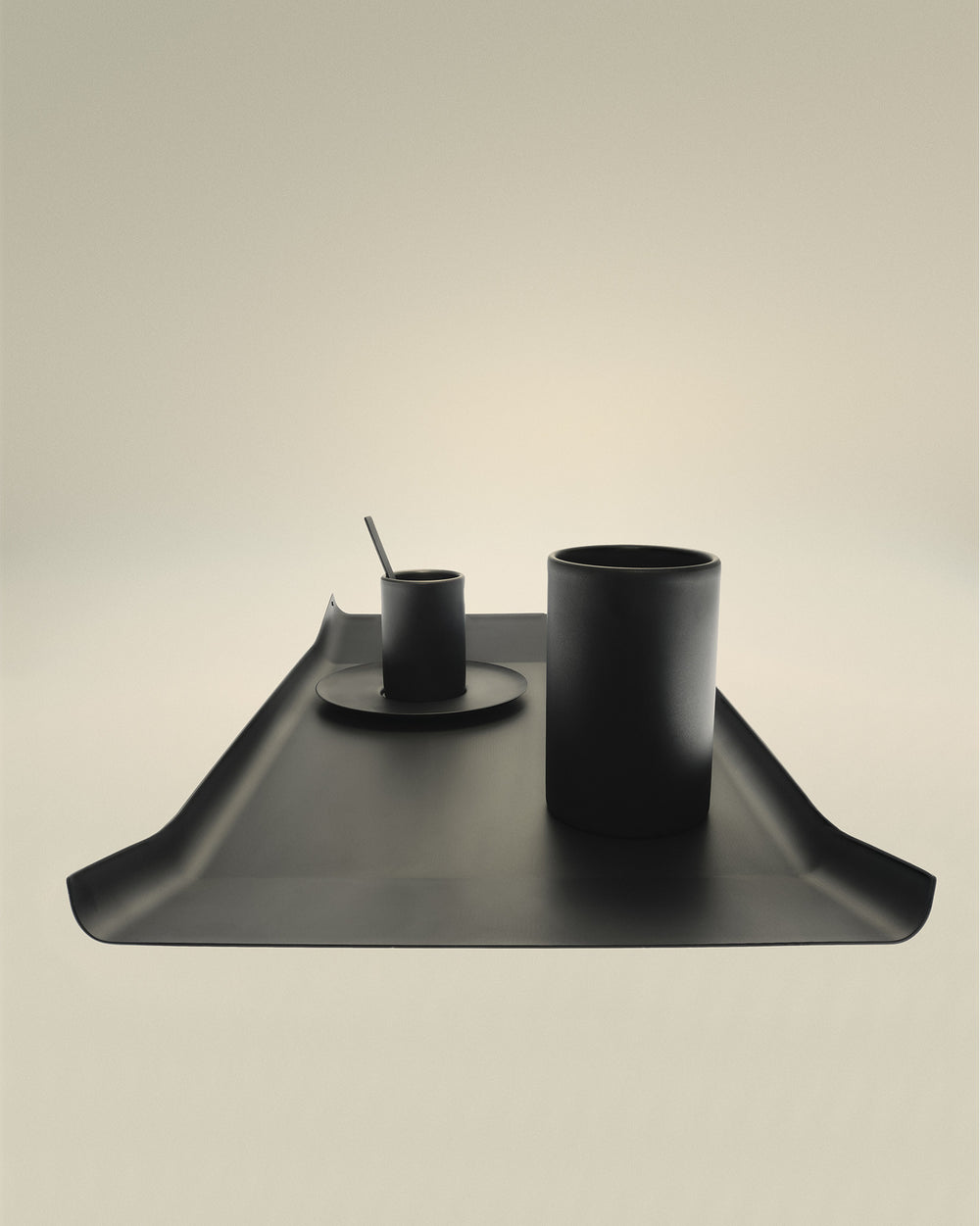 Modern matte black cylindrical cups by Alessi, arranged with a spoon on a matching tray.