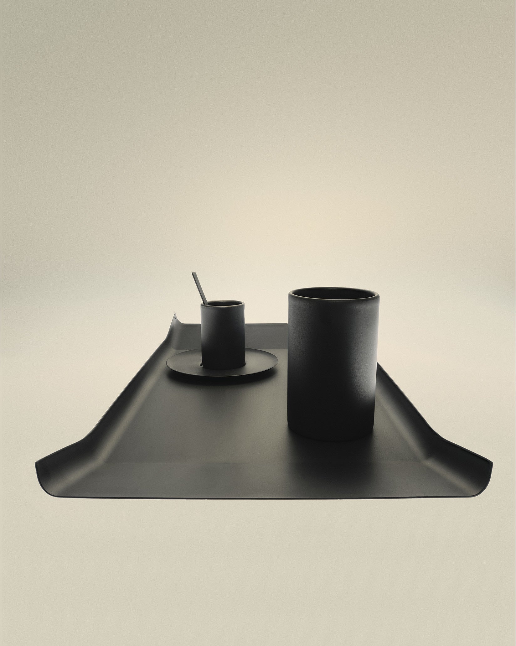 Modern matte black cylindrical cups by Alessi, arranged with a spoon on a matching tray.