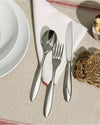 Polished stainless steel Mami table fork by Alessi, resting on a white napkin with other cutlery and a striped tablecloth.