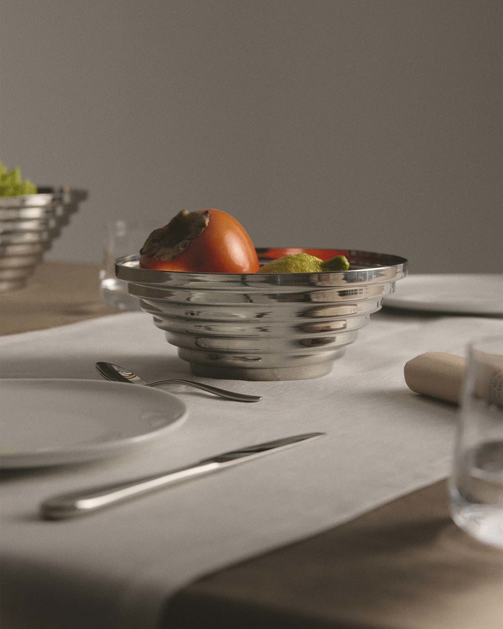 Silver-toned Maya fruit bowl by Alessi with a ribbed design, holding fruit.