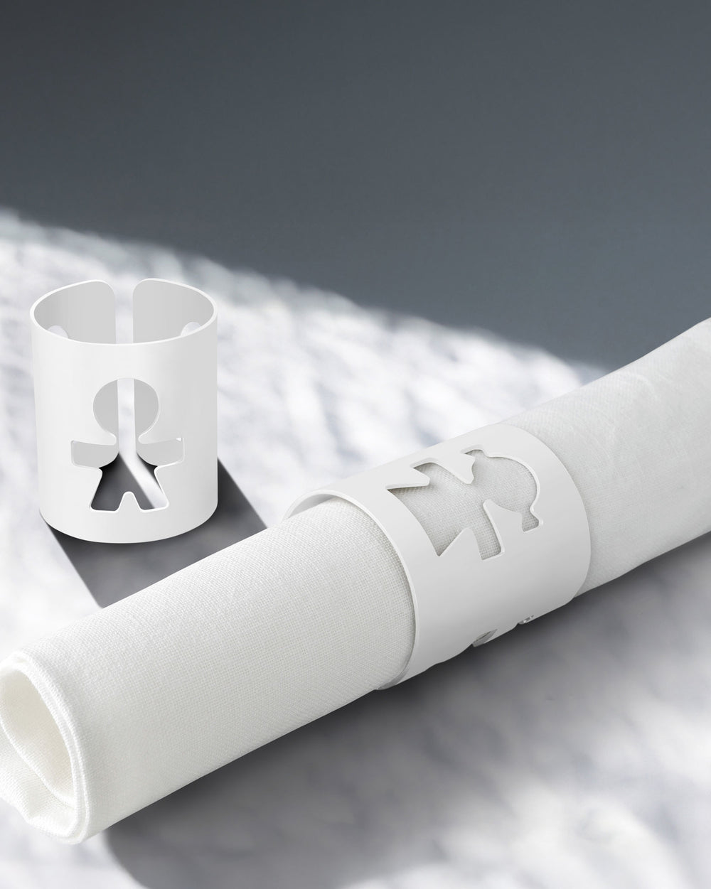 White napkin holders by Alessi with a human figure cut-out design, one holding a rolled white napkin.