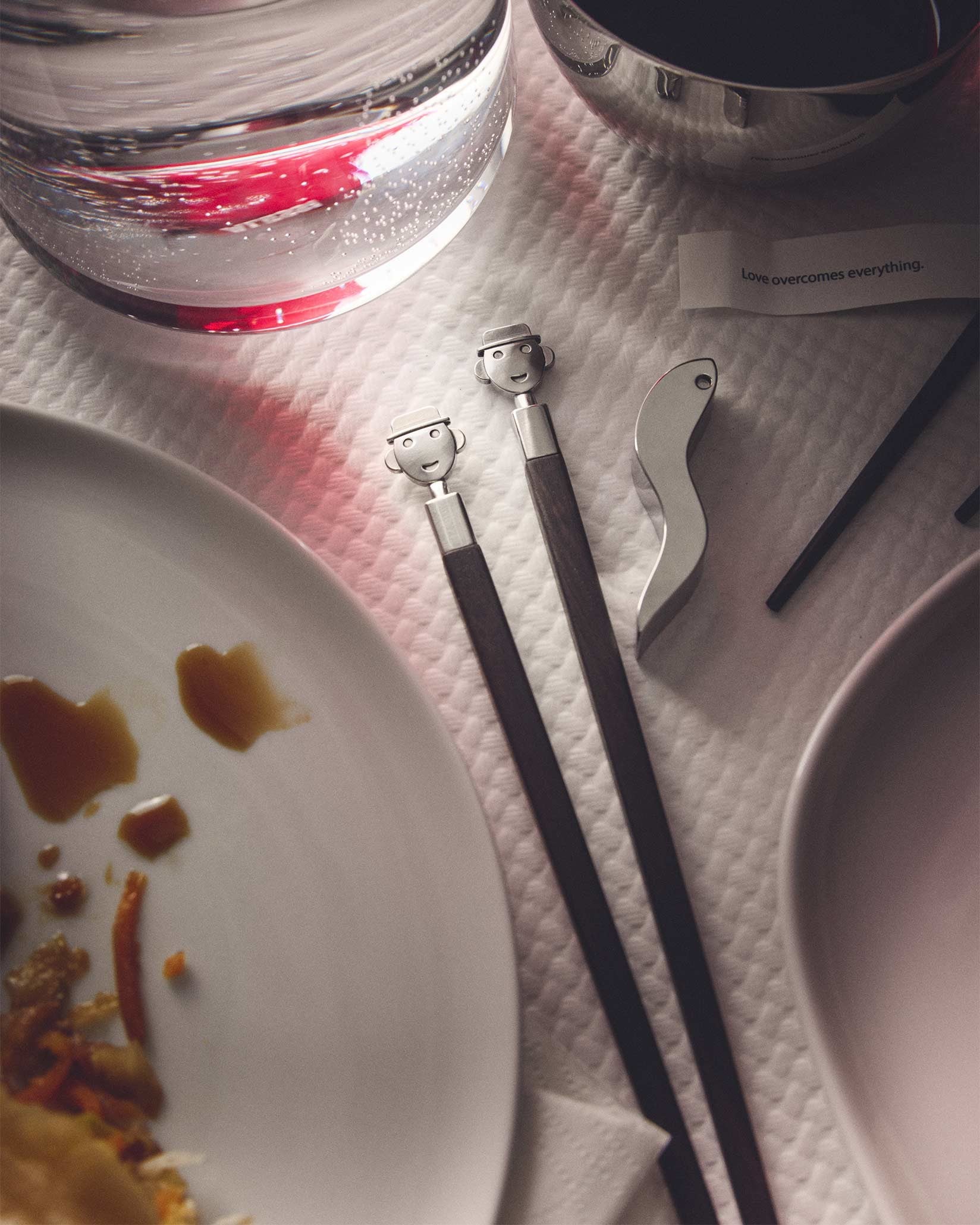 Designer chopsticks by Alessi with smiling character heads and dark wood handles, part of a sushi set.