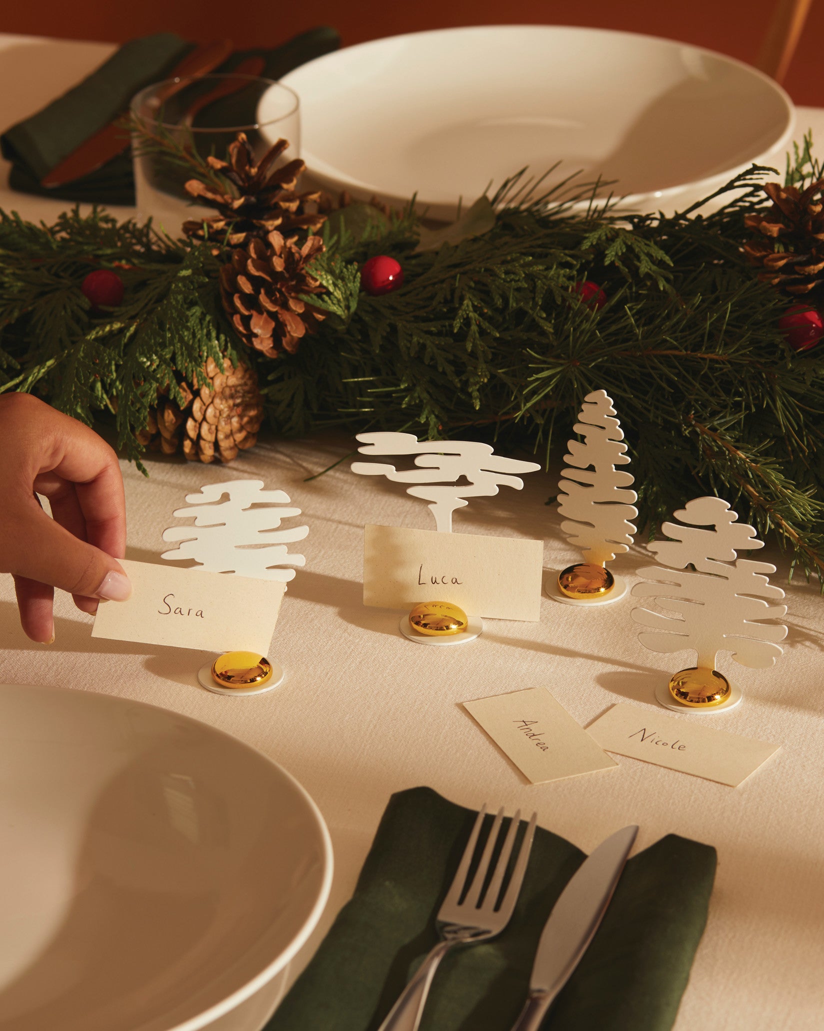 White tree place markers with gold bases by Alessi, holding name cards on a festive table setting.