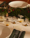 Silver-toned metallic tree place markers by Alessi, holding name cards on a festive table with pine cones.