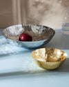 Two faceted serving bowls by Alessi, one large in silver with a red apple, one smaller in gold.