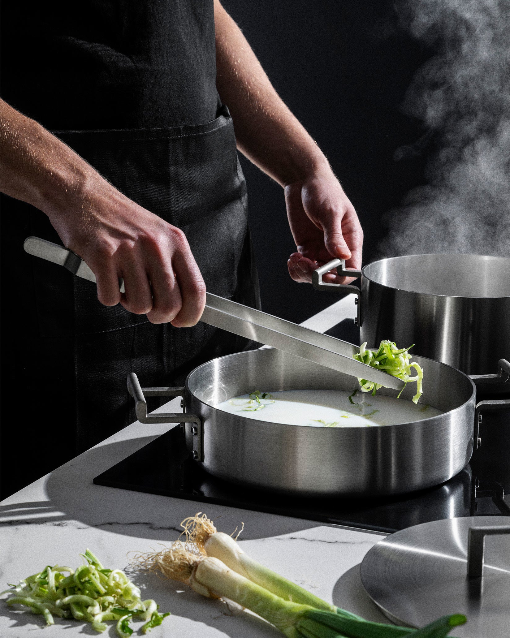 Stainless steel Convivio kitchen tongs by Alessi in use, adding chopped green vegetables to a pot.
