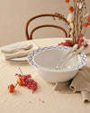 White ceramic salad serving bowls by Alessi with blue geometric diamond pattern rims, nested with two silver serving utensils.