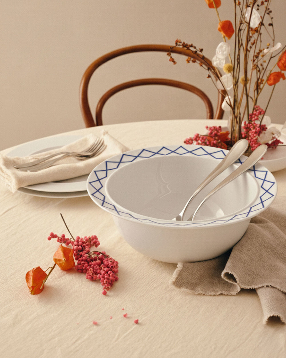 White ceramic salad serving bowls by Alessi with blue geometric diamond pattern rims, nested with two silver serving utensils.