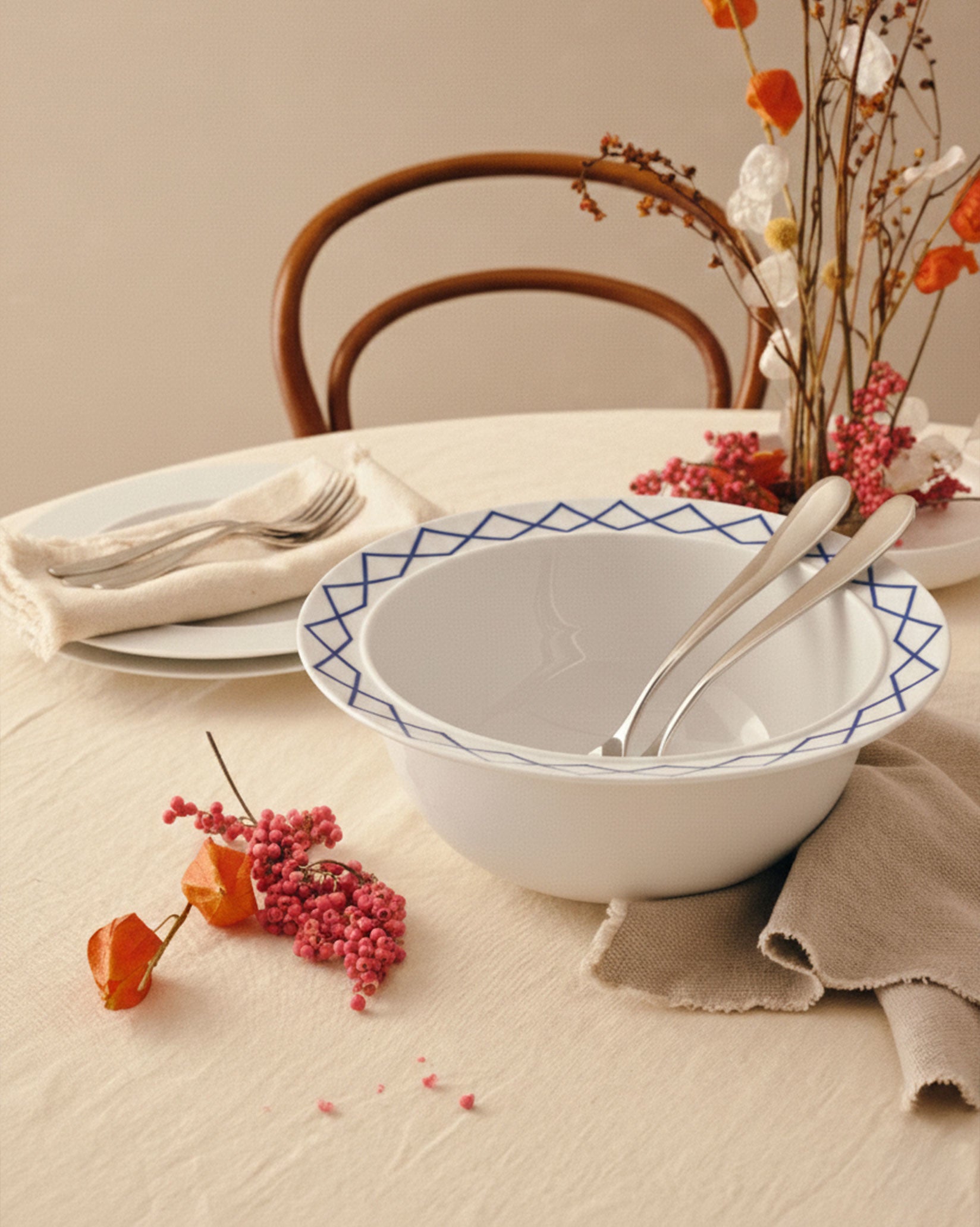 White ceramic salad serving bowls by Alessi with blue geometric diamond pattern rims, nested with two silver serving utensils.