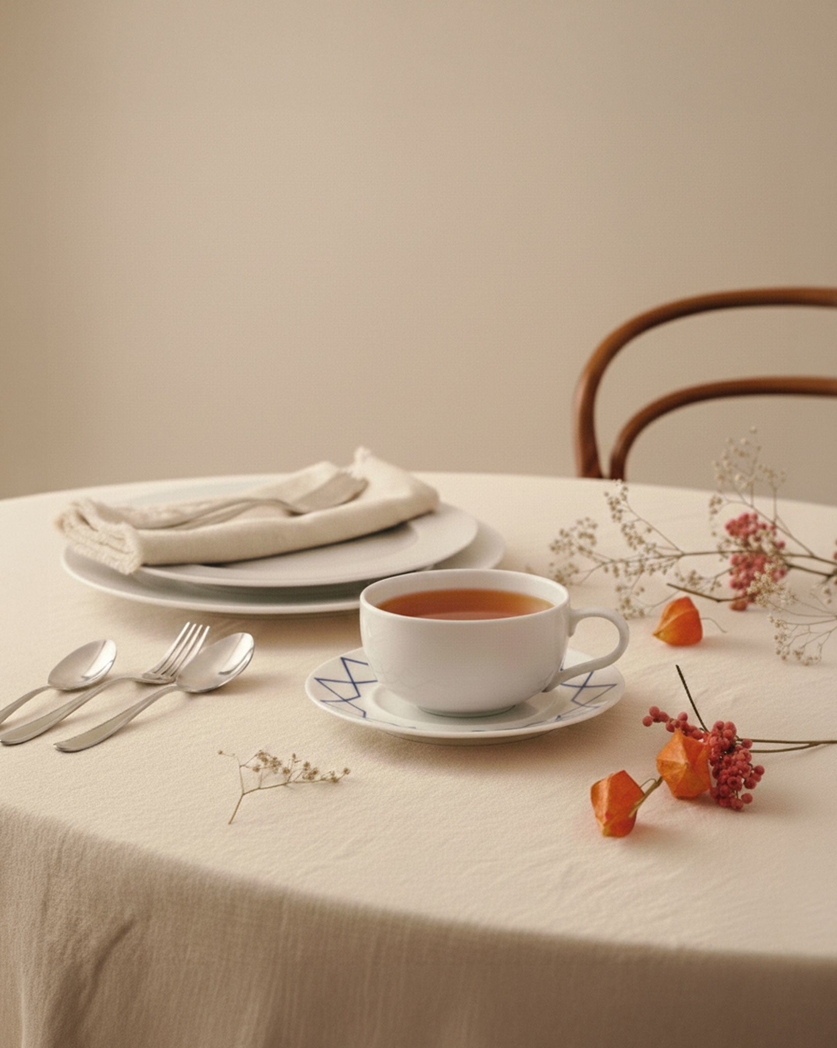 White ceramic saucer by Alessi with blue geometric patterns, holding a teacup on a beige tablecloth with flowers.
