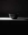 Black metal bowl by Alessi with two etched lines near the rim, dramatically lit from below.