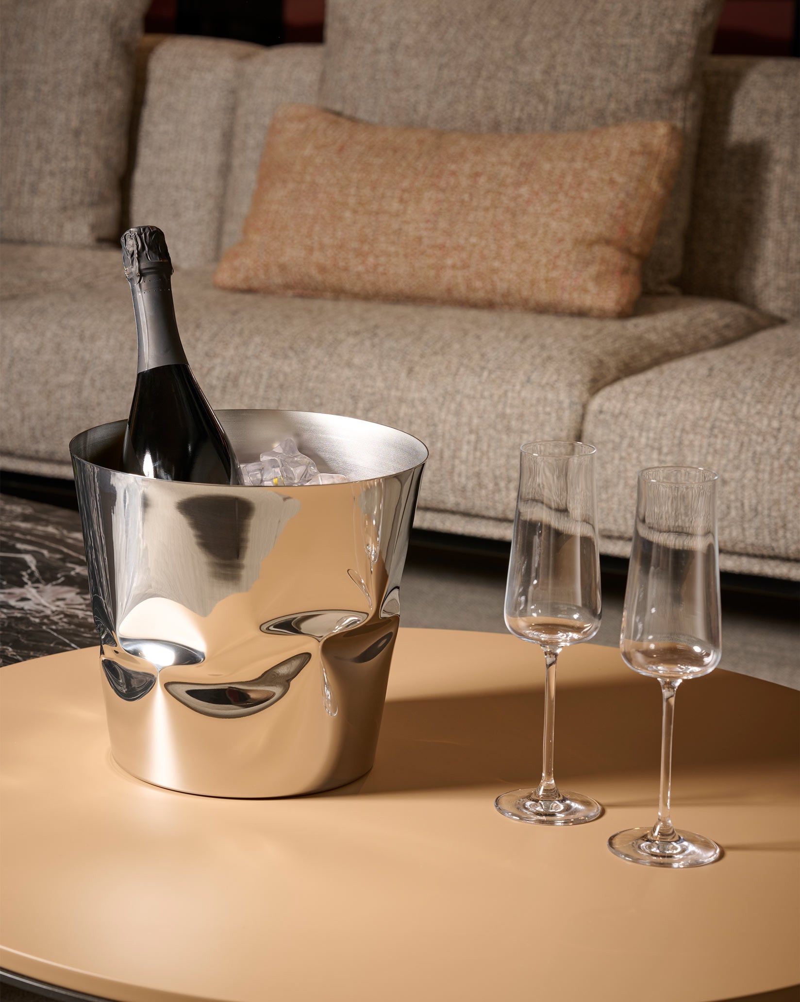 Silver crumpled design wine cooler by Alessi, holding a champagne bottle and ice, with two empty flutes.