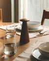 Dark brown wooden salt, pepper and spice grinder by Alessi, conical with stacked rings, on a dining table.
