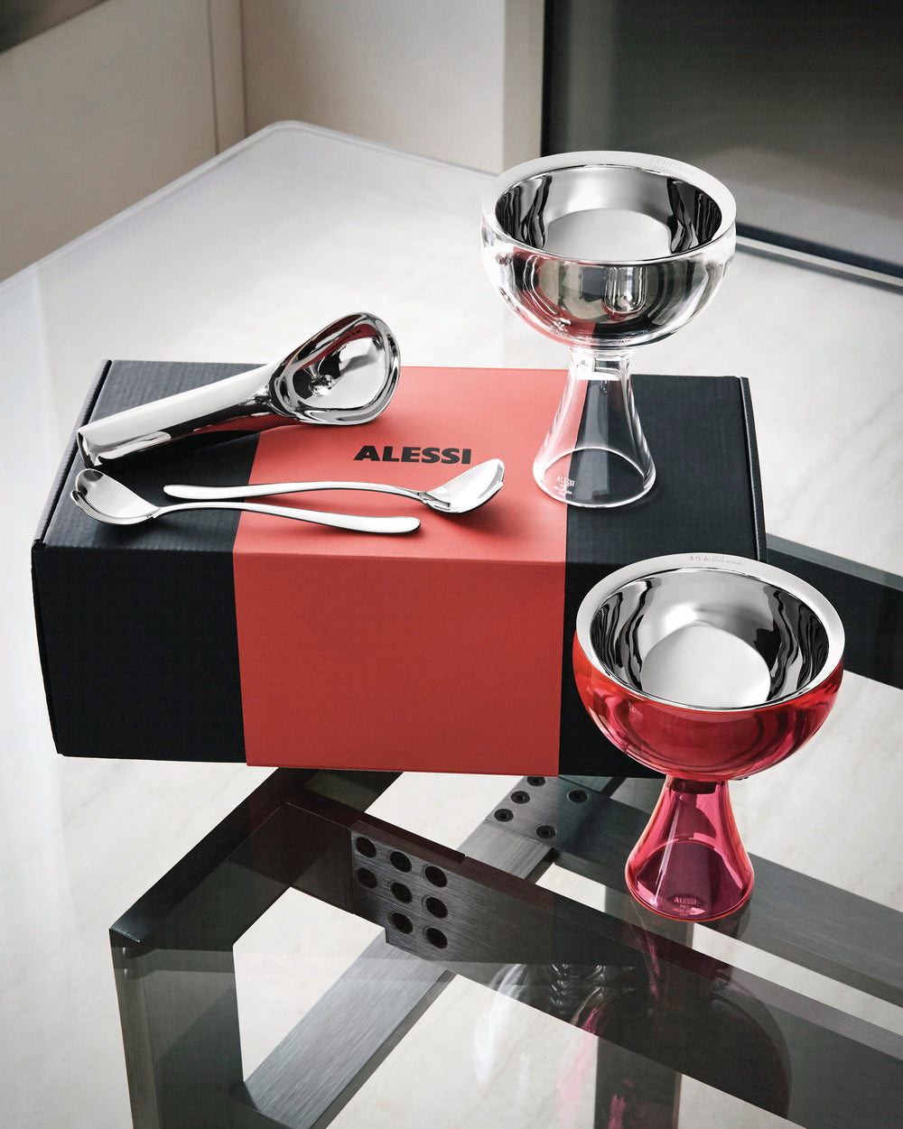 Ice cream gift set by Alessi with a scoop, two spoons, and two dessert bowls, displayed on a red and black box.
