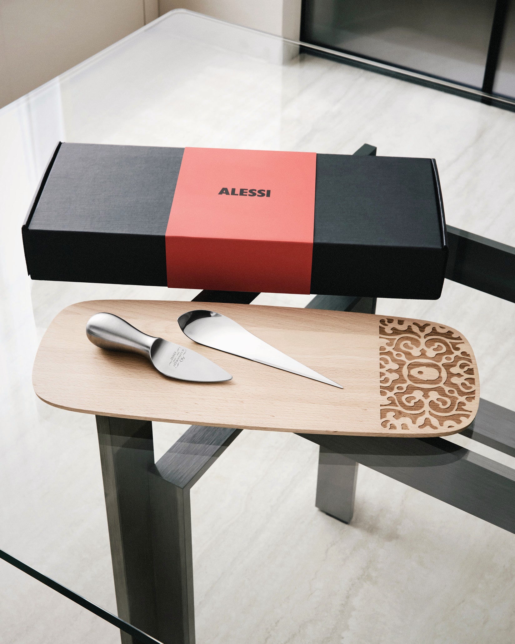 Black and red cheese gift set by Alessi with two silver tools and a carved wooden board.