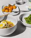 White Itsumo salad serving bowls by Alessi, shown filled with ramen and edamame on a light table.