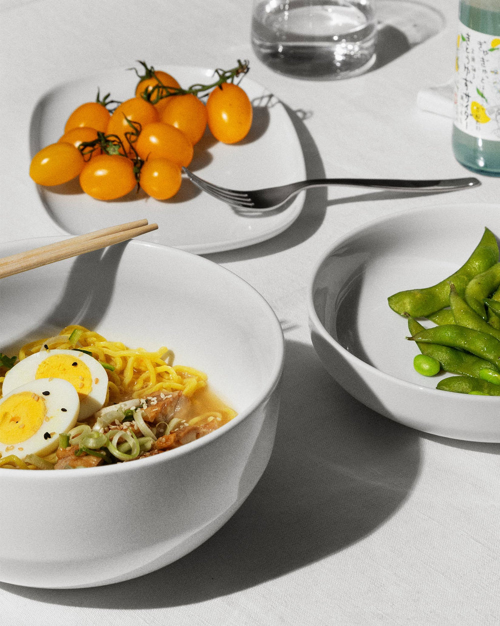 White Itsumo salad serving bowls by Alessi, shown filled with ramen and edamame on a light table.