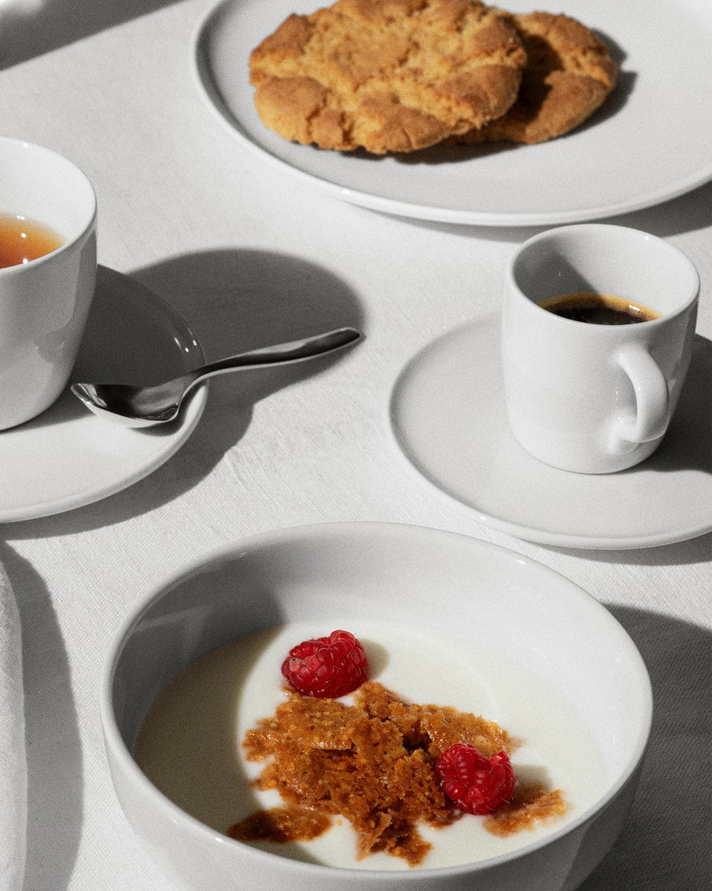 White ceramic tea and coffee set by Alessi with a tea cup, espresso cup, and bowl filled with yogurt and berries.