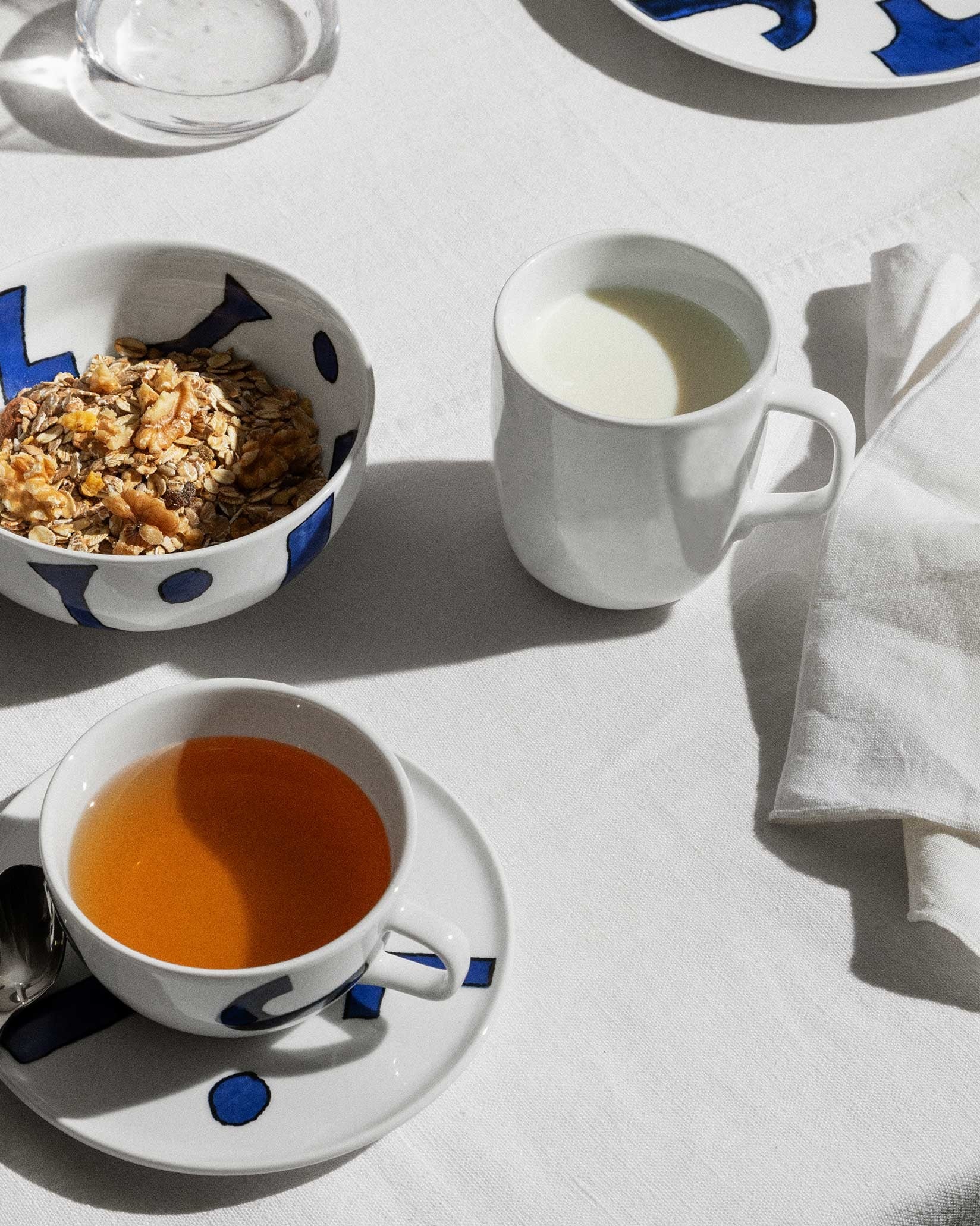 White ceramic teacup, saucer, mug, and bowl by Alessi with abstract blue patterns.