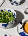 White Yunoki ware table set by Alessi featuring abstract blue patterns, with bowls of green salad and orange soup.
