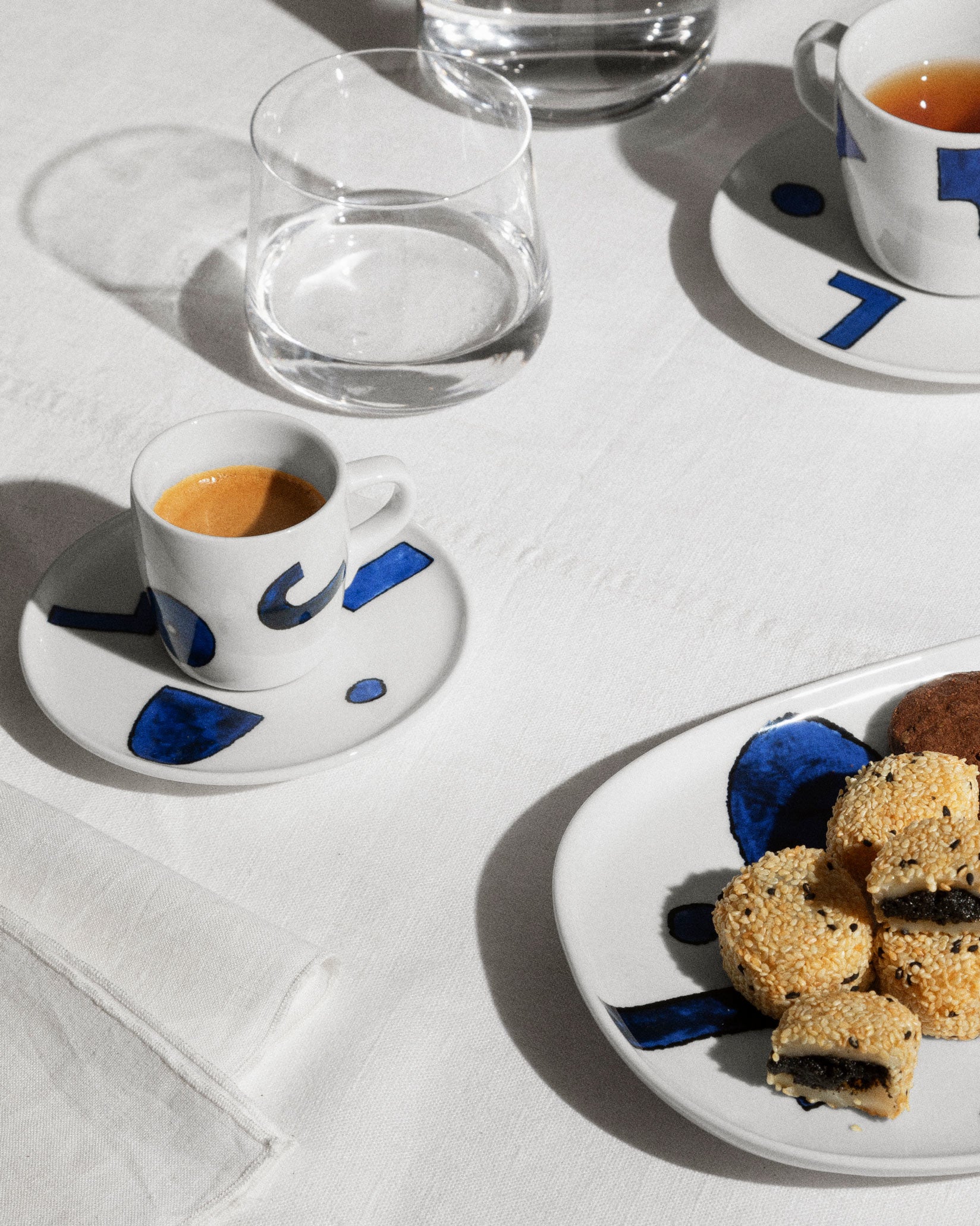 White ceramic table set by Alessi with hand-painted blue abstract patterns on a white tablecloth.