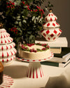 White ceramic cake stand with red radial stripes by Alessi, holding a Christmas cake amidst festive decor.