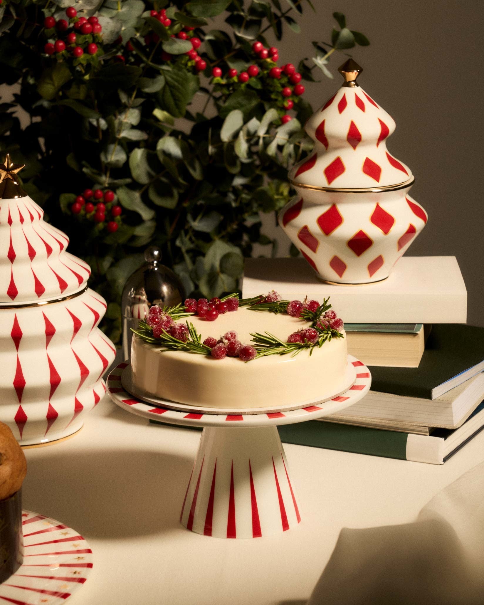 White ceramic cake stand with red radial stripes by Alessi, holding a Christmas cake amidst festive decor.
