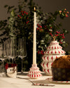 White and red ceramic candlestick by Alessi, with a Christmas tree shape and diamond pattern, holding a lit cream taper candle.