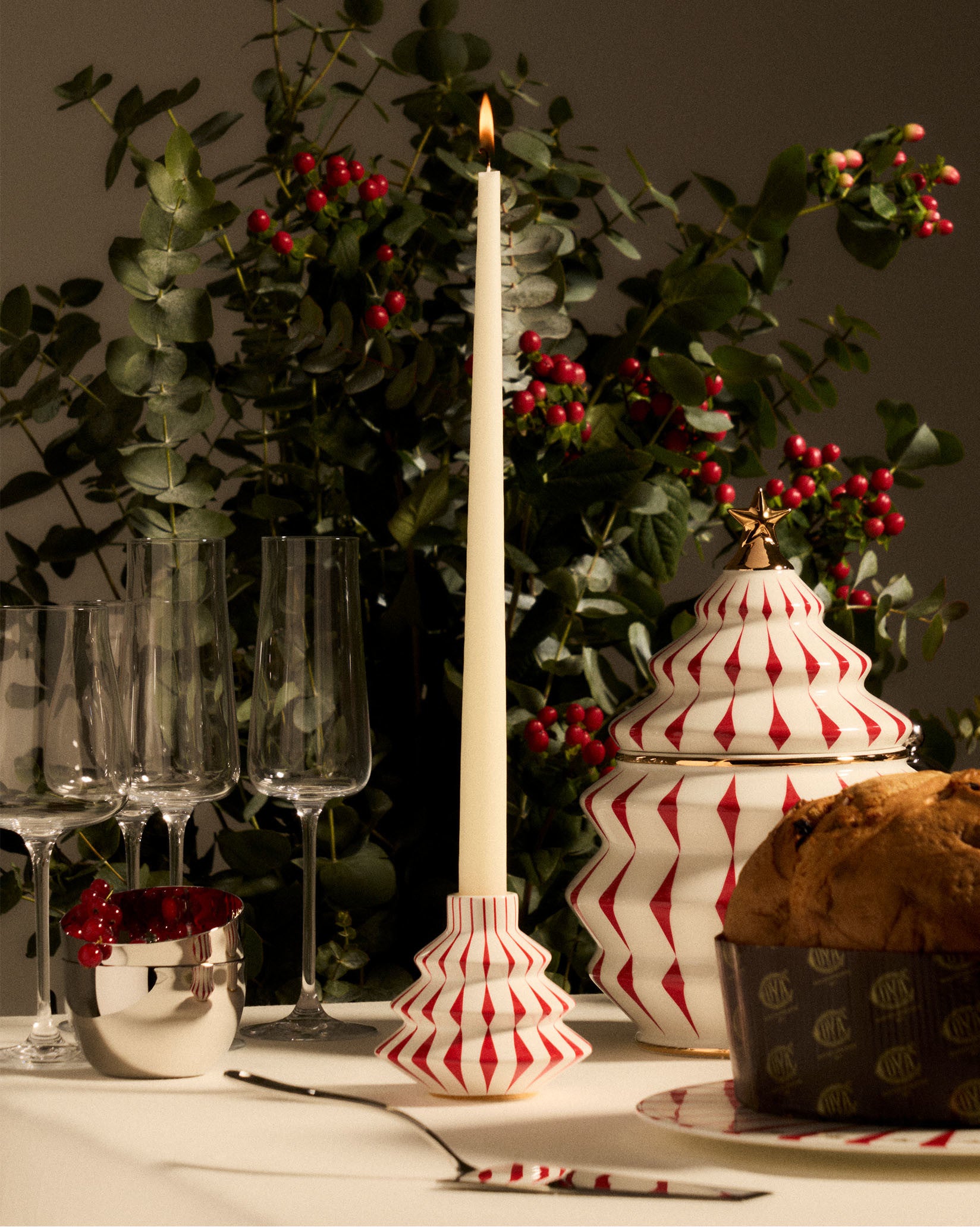 White and red ceramic candlestick by Alessi, with a Christmas tree shape and diamond pattern, holding a lit cream taper candle.