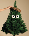 White googly eyes and woven ring Christmas tree ornaments by Alessi, on a green artificial tree, a hand adjusting the top.