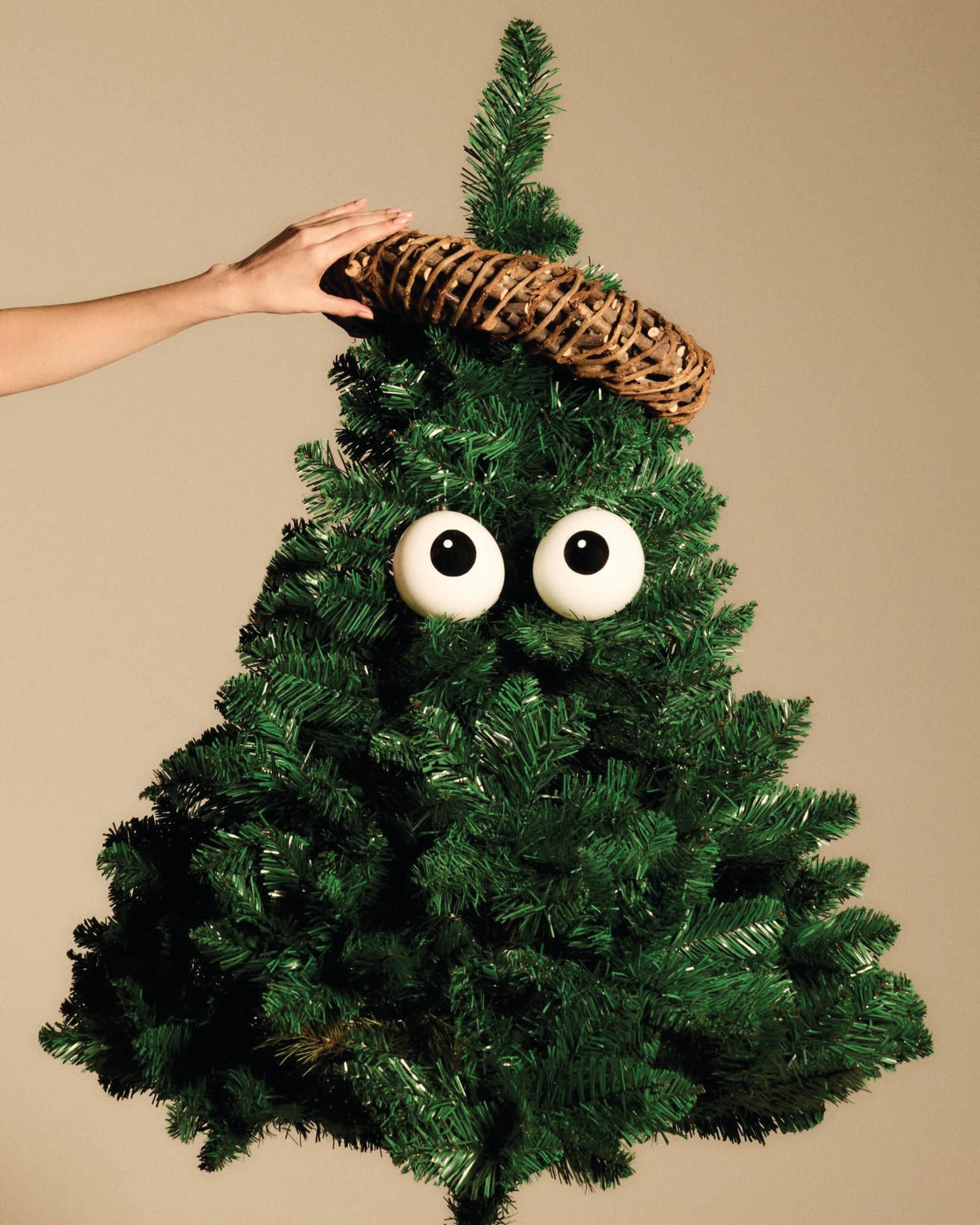 White googly eyes and woven ring Christmas tree ornaments by Alessi, on a green artificial tree, a hand adjusting the top.