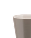 Cropped view of a light grey tapered ceramic cup by Alessi, with a matte exterior and glossy interior.