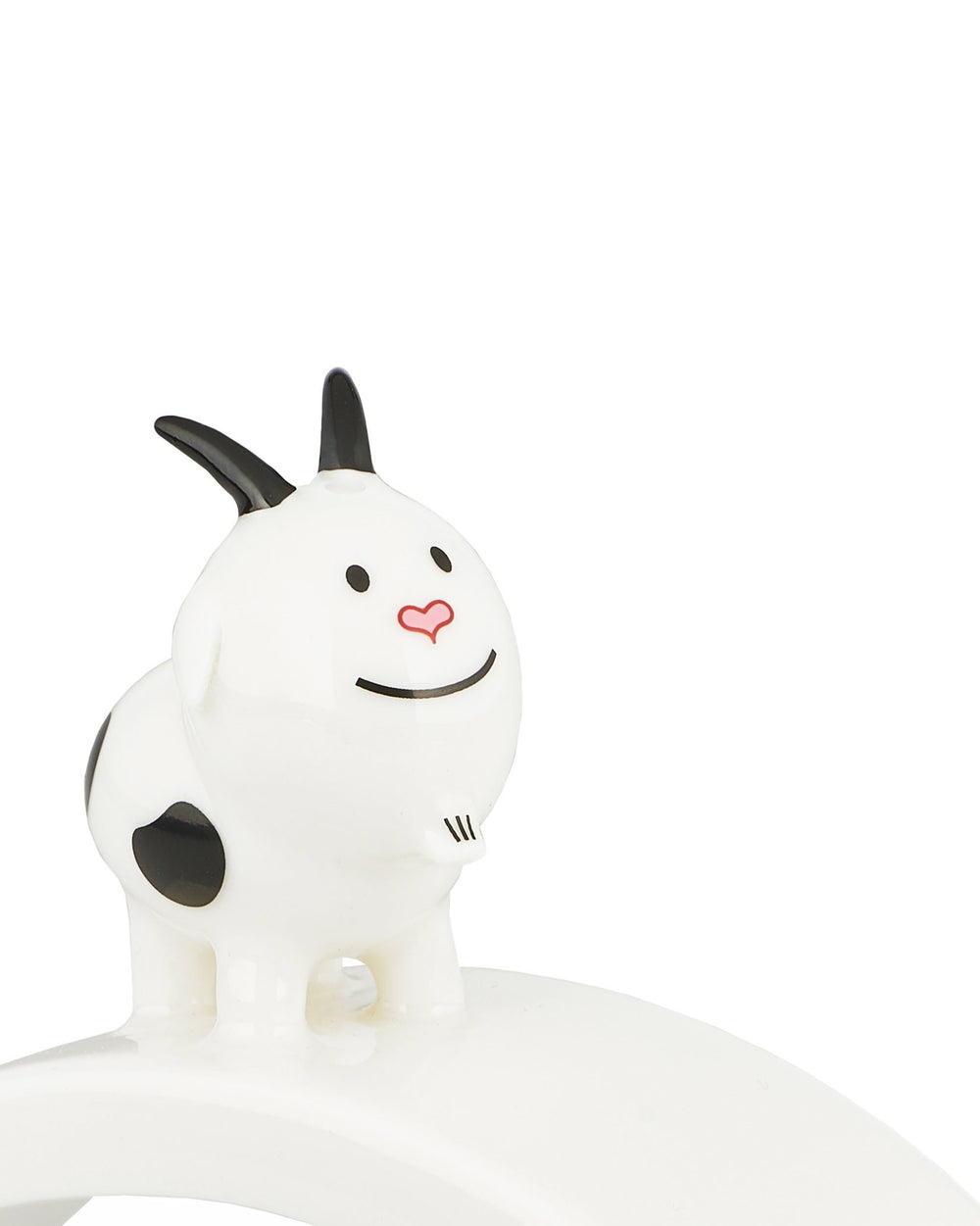 White ceramic ornamental figurine by Alessi, a smiling cartoon goat with black horns, spots, and a pink heart nose.