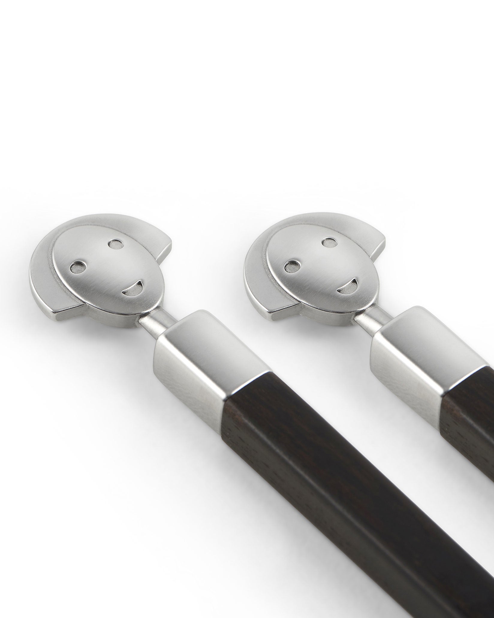 Two brushed stainless steel and dark wood sushi sticks by Alessi, featuring smiling character faces.