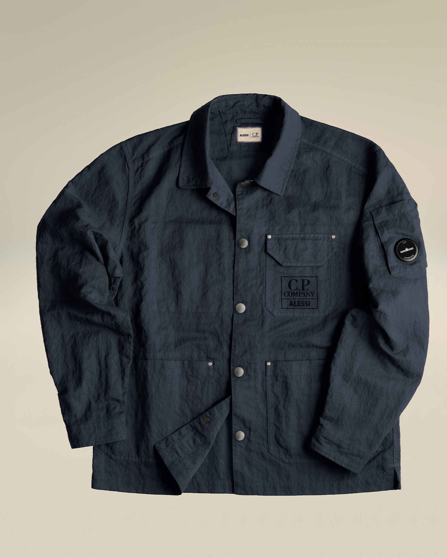 Navy blue crinkled utility jacket by Alessi, with button closure and visible C.P. Company logos.