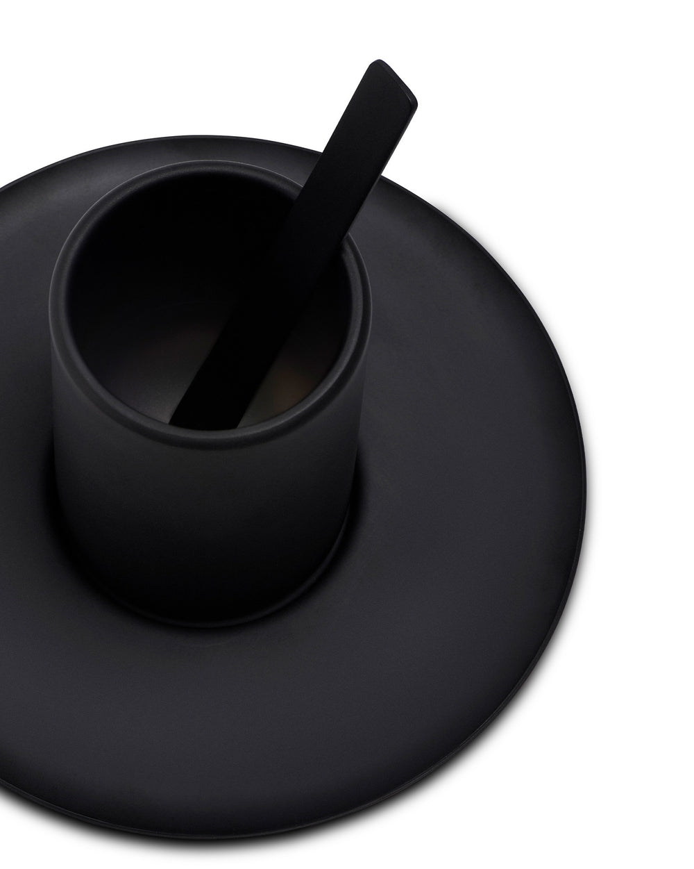 Black matte cup by Alessi with a flat stirrer on a matching round saucer, angled view.