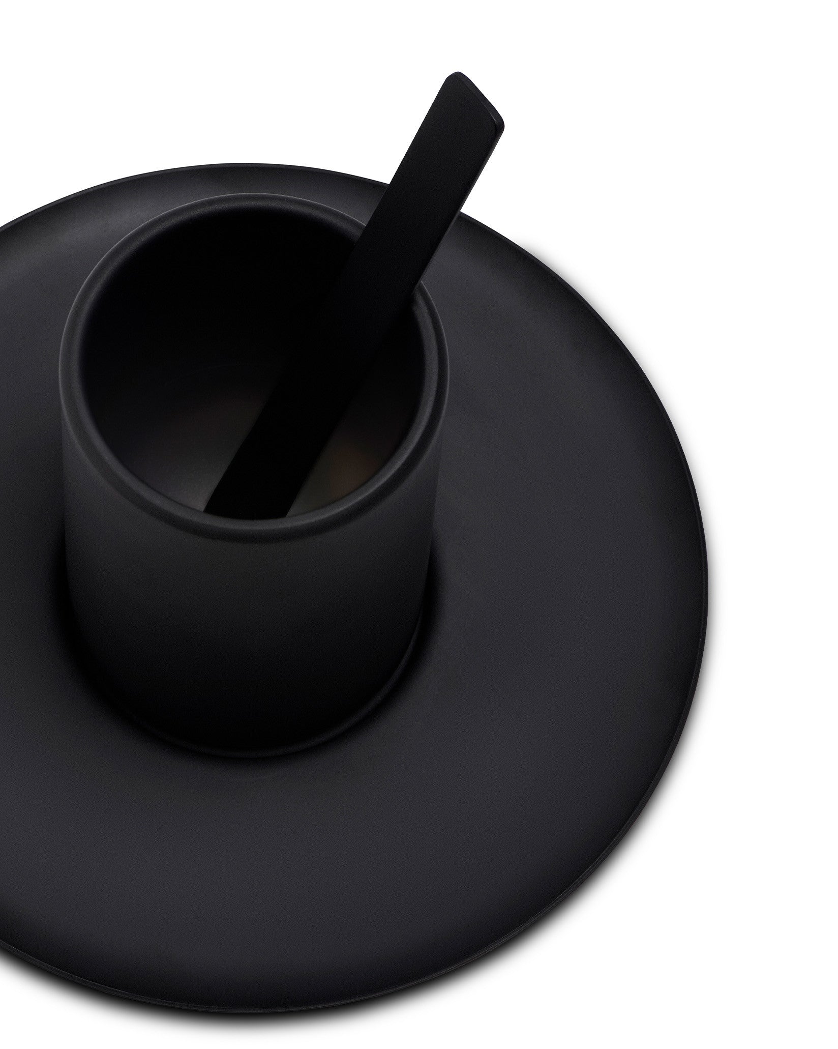 Black matte cup by Alessi with a flat stirrer on a matching round saucer, angled view.
