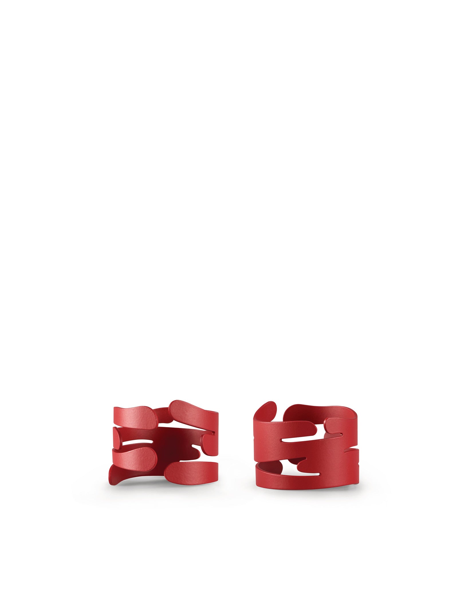 Two red Barkring napkin holders by Alessi with an abstract, flowing design.