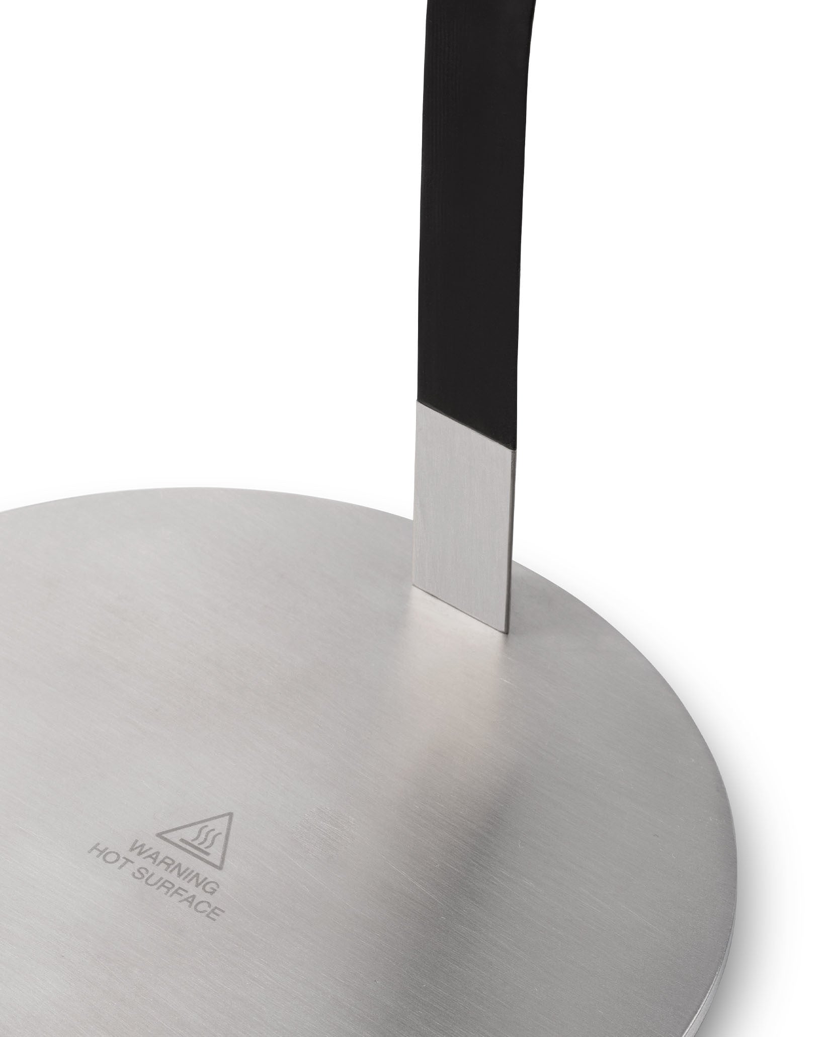 Brushed silver metal warmer base by Alessi, with a black upright element and "WARNING HOT SURFACE" text.