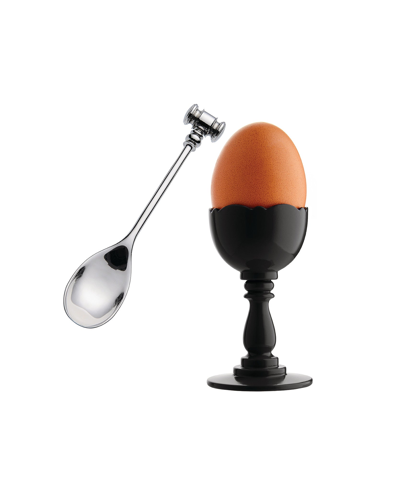 Black egg cup by Alessi with a wavy rim and ornate pedestal, holding a brown egg, beside a silver spoon with a gavel handle.